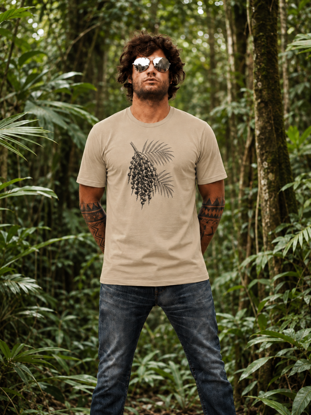 Renan wearing the Son of Nature Acai botanical tee in sandstone, charcoal acai palm-and-berry engraving across the chest, standing in dense green Kauai jungle