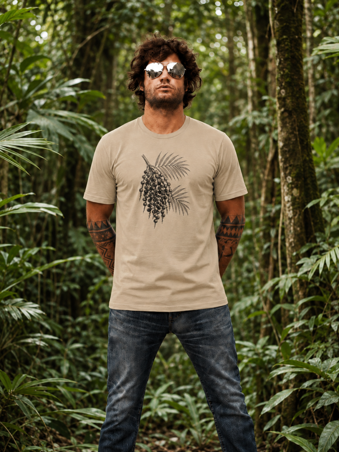 Renan wearing the Son of Nature Acai botanical tee in sandstone, charcoal acai palm-and-berry engraving across the chest, standing in dense green Kauai jungle