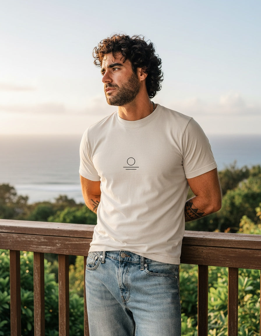 Renan wearing the Son of Nature S.O.N. emblem tee in ivory, charcoal sun-over-water mark on the chest, golden-hour Kauai ocean overlook
