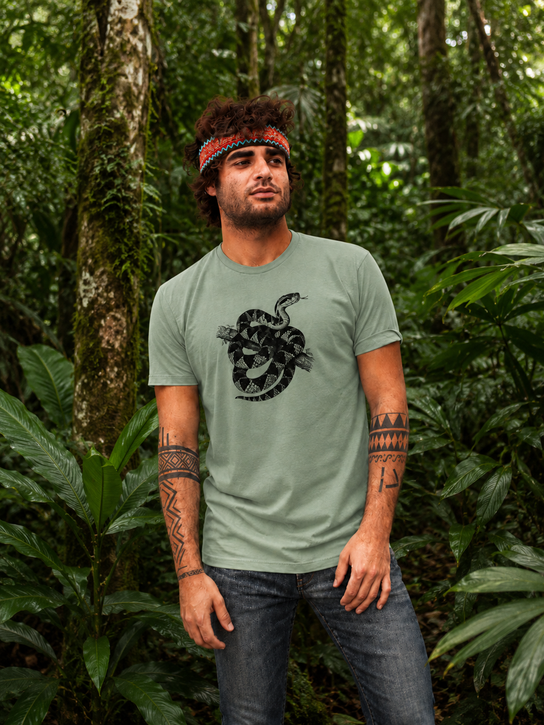 Renan wearing the Son of Nature Surucucu bushmaster tee in bay, charcoal bushmaster coiled on a branch on the chest, standing in a lush green jungle